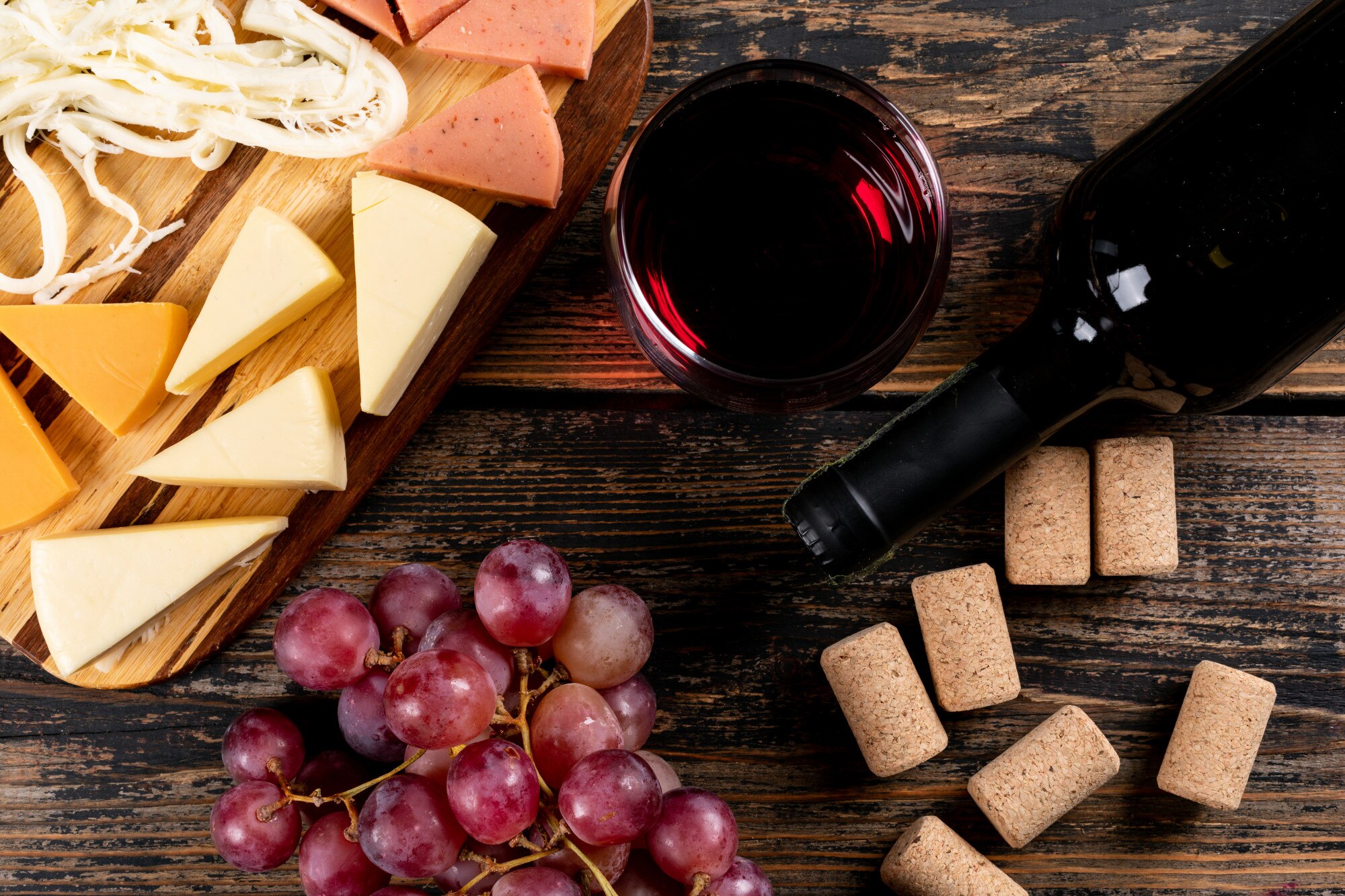 vista-superiore-di-vino-rosso-con-l-uva-e-il-formaggio-sul-tagliere-sull-orizzontale-di-legno-scuro_176474-4508